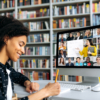 View over shoulder of a mixed race clever female student at a computer screen with a female teacher and students. Teacher conducts online lecture, female student takes notes. Online training,video call-806