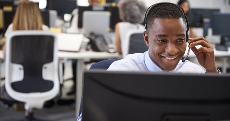 Young man working at computer with headset in busy local council office