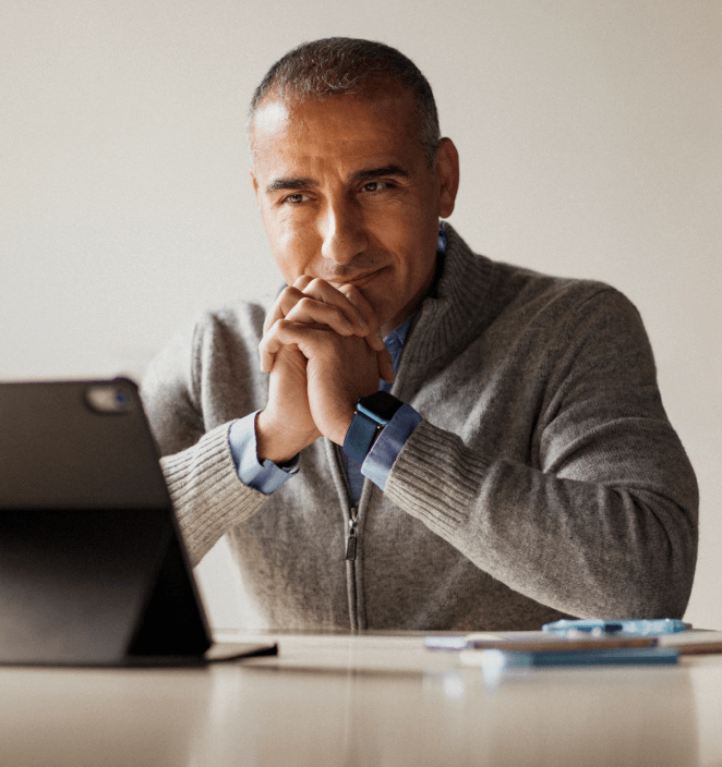 A man with clasped hands in front of his laptop